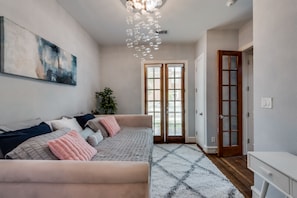 A modern bedroom with a sofa, a large abstract painting, a chandelier, and a view through a glass door.