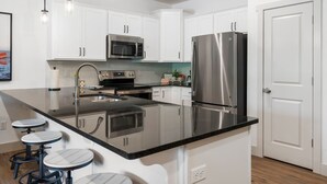 A modern kitchen with white cabinets, stainless steel appliances, a black countertop, and bar stools. - New Lakeside Haven - Picturesque (Branson)