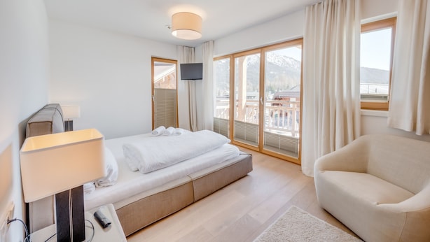 A modern hotel room with a bed, a sofa, a TV, and a balcony with a mountain view. - Pool-chalet - Zentral in Seefeld (Seefeld in Tirol)