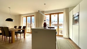 A modern kitchen with a central island, a dining area with a wooden table and chairs, and large sliding glass doors leading to a balcony. - Pool-chalet - Zentral in Seefeld (Seefeld in Tirol)