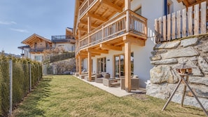 Una casa moderna con balcón de madera, pared de piedra y zona de estar exterior.