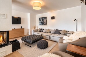 Una sala de estar moderna con chimenea, un conjunto de sofás, un televisor de pantalla plana y un cuadro en la pared.