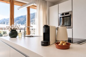 A modern kitchen with a coffee maker, a kettle, and a bowl of bread on the counter.