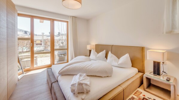 A hotel room with a large bed, two bedside lamps, a nightstand, and a view of the outdoors through a large window. - Pool-chalet - Zentral in Seefeld (Seefeld in Tirol)