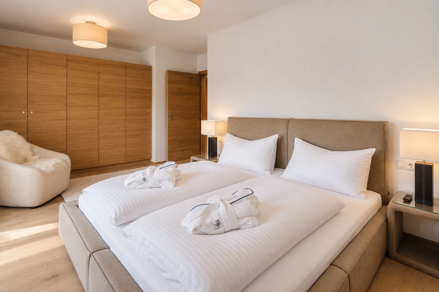 Ein Hotelzimmer mit einem großen Bett, zwei Nachttischen mit Lampen, einem Holzschrank und einem gemütlichen Sessel.
