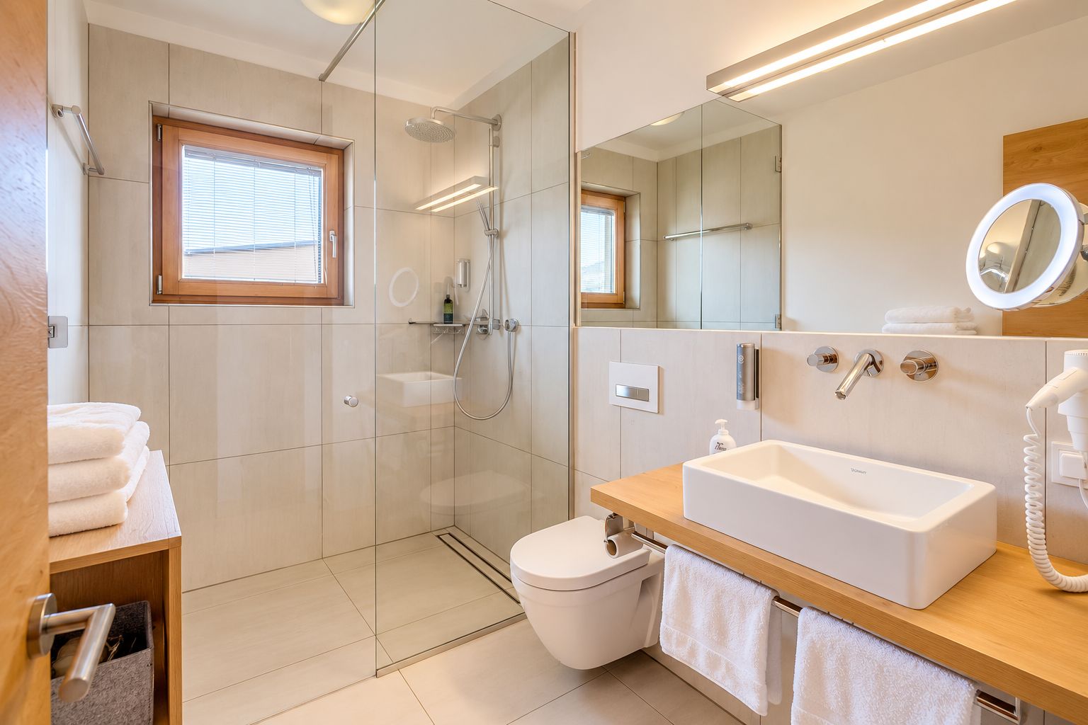 A modern bathroom with a glass-enclosed shower, a white sink, a mirror, and a towel rack.