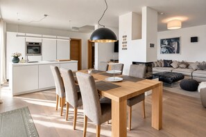 A modern kitchen with a built-in oven and a dining area with a wooden table and grey upholstered chairs.