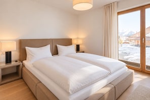 Habitación de hotel con una cama grande, dos mesitas de noche y un ventanal con vistas a montañas nevadas.