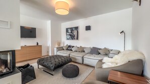 A modern living room with a sofa, ottoman, and a flat-screen TV mounted on the wall. - Pool-chalet - Zentral in Seefeld (Seefeld in Tirol)
