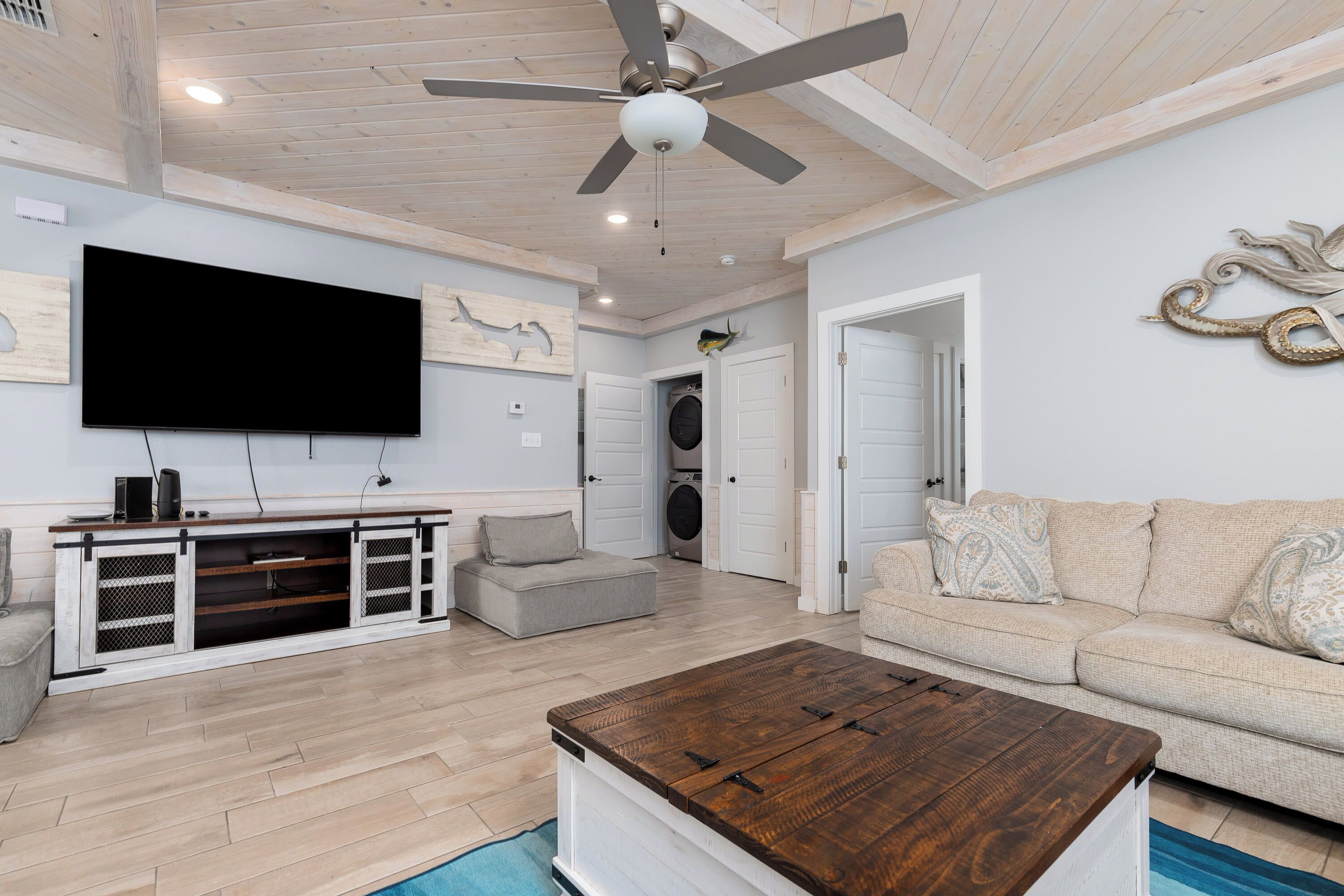 A living room with a flat-screen TV, wooden ceiling, and a ceiling fan.