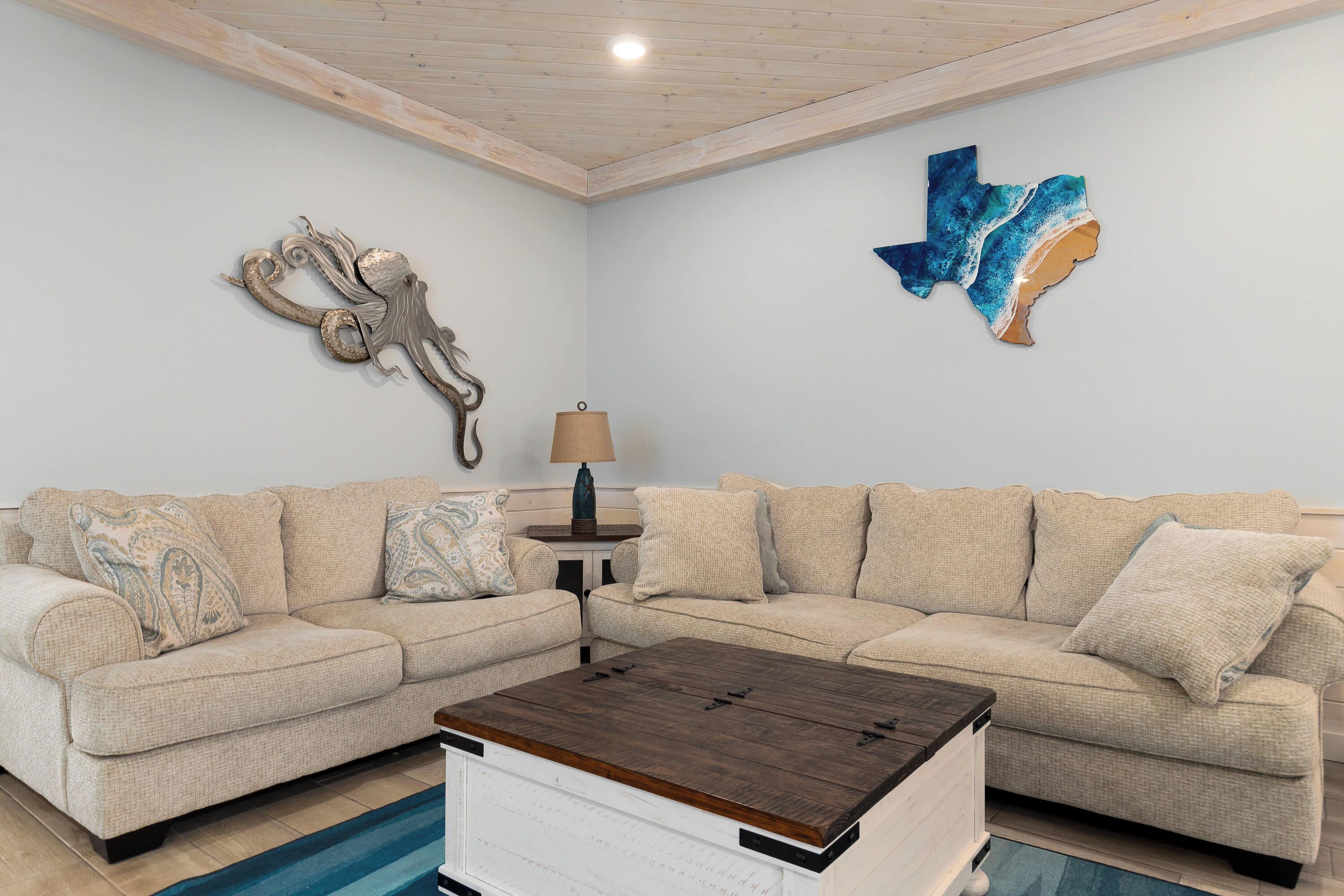 A living room with a beige sectional sofa, a wooden coffee table, and a lamp on a small table.