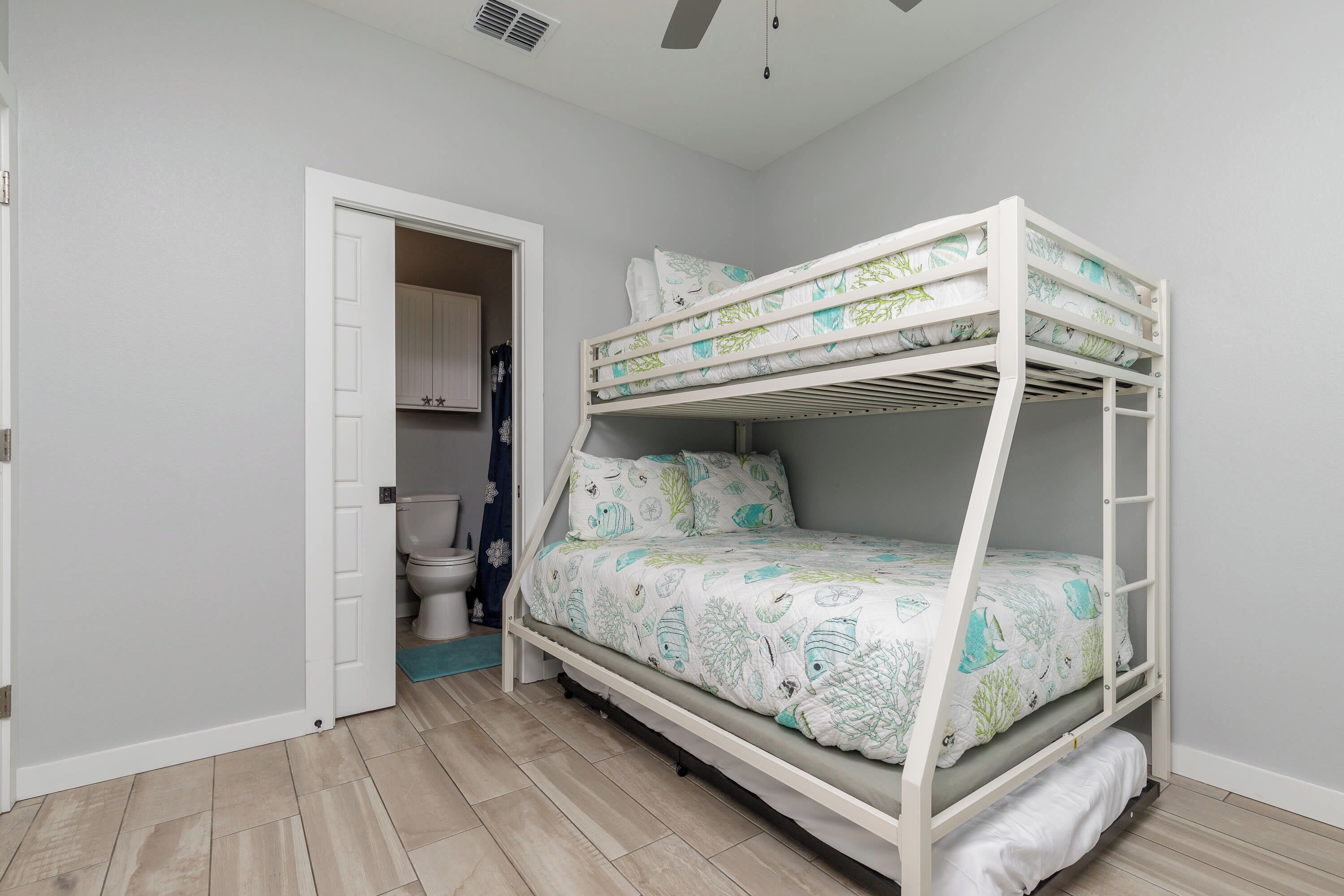 Un lit superposé avec une structure blanche et une couvre-lit à motifs, une porte blanche et un plancher en bois de couleur claire.