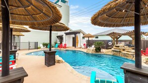 A swimming pool with thatched umbrellas, colorful chairs, and a stone waterfall feature. - Modern Comfort, 3 Bedroom, Pets (Port Aransas)