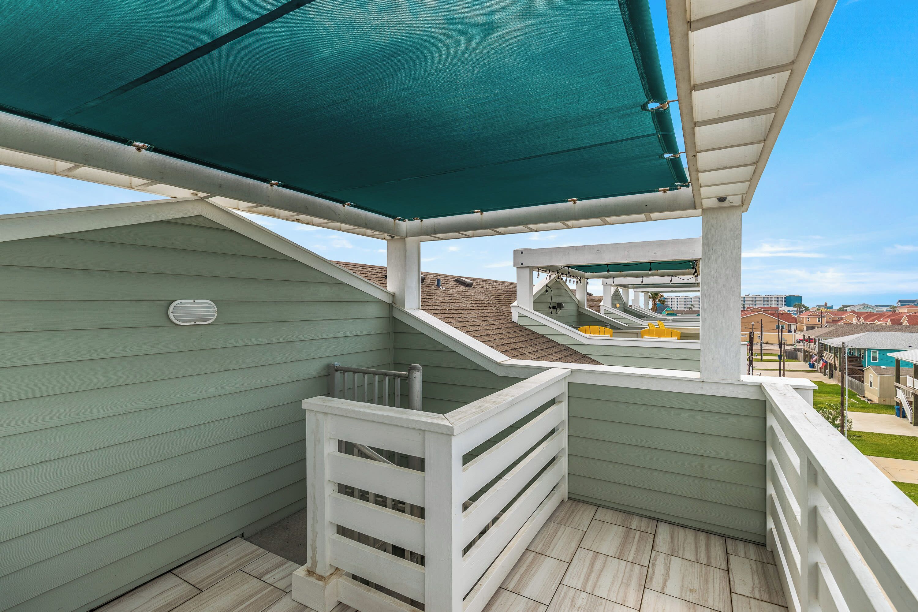 A balcony with a green awning, white railings, and a view of a residential area.