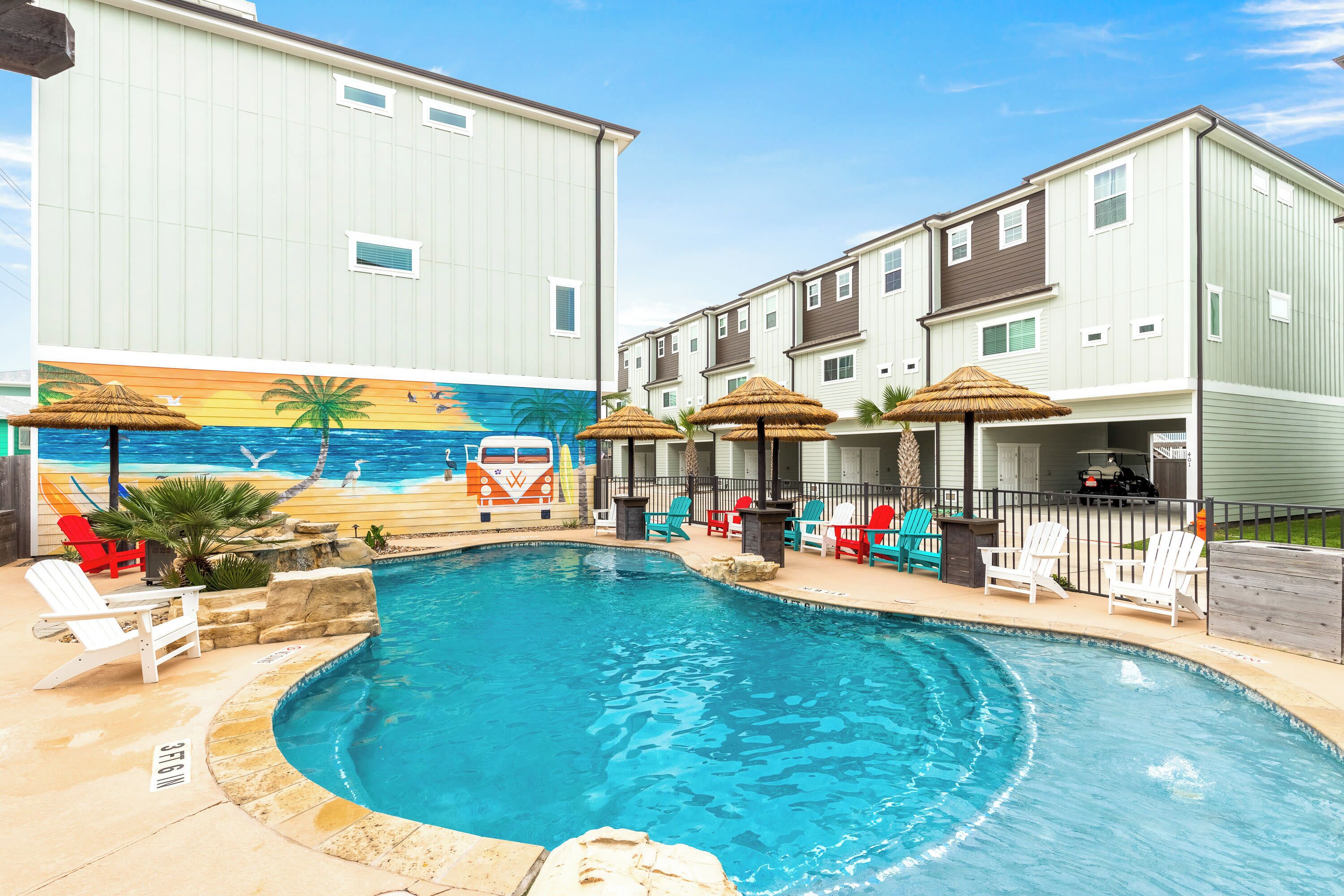 A swimming pool with lounge chairs and umbrellas, surrounded by buildings with a mural of a beach scene.