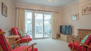A living room with two red chairs, a television on a wooden stand, and a sliding glass door leading to a patio. - 2 bedroom accommodation in Reepham (Reepham)