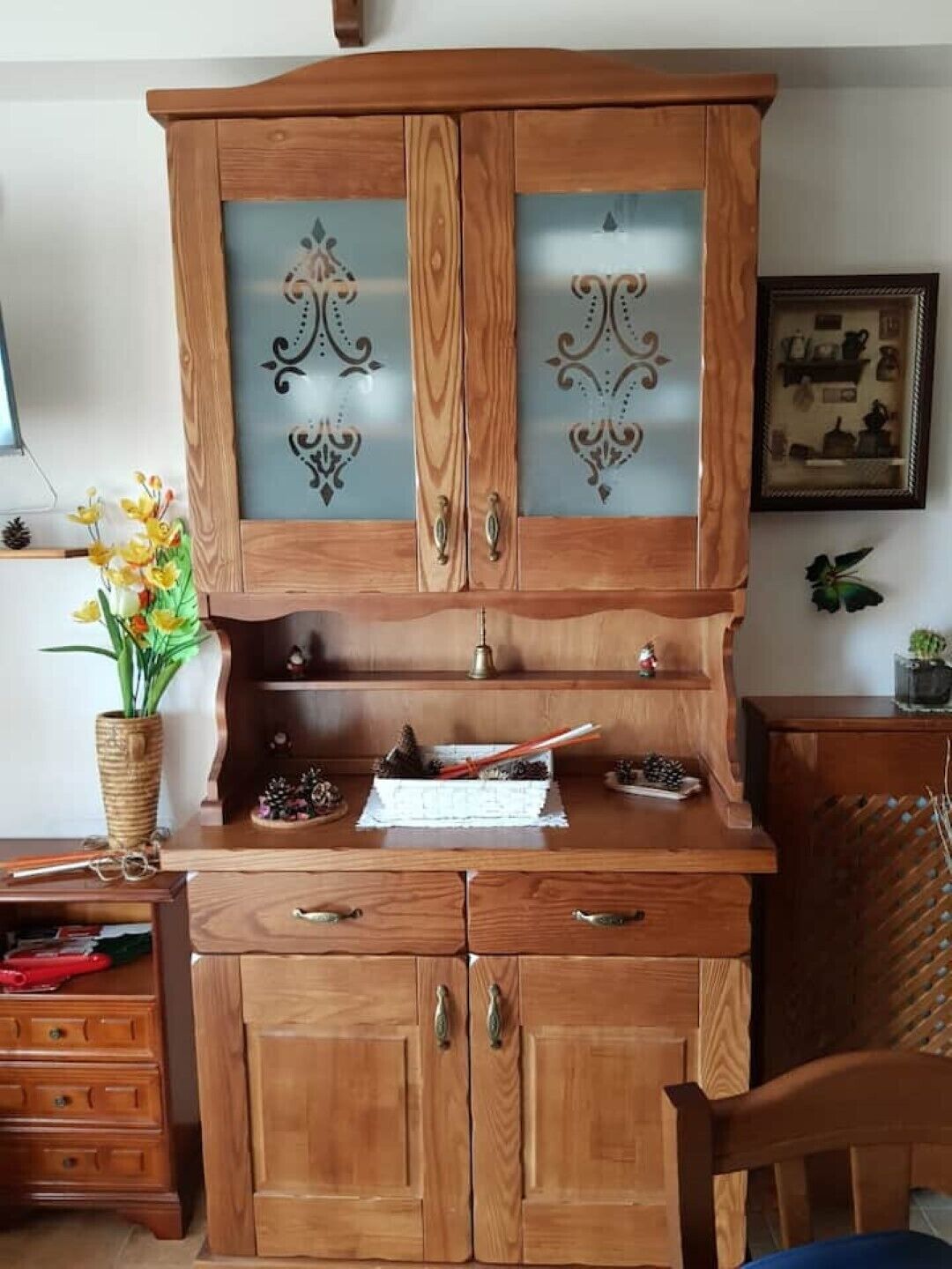 A wooden cabinet with glass doors and a shelf, containing decorative items and a small plant.