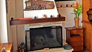Uma lareira com design rústico, um parapeito de madeira com objetos decorativos e um pequeno armário de madeira à direita.