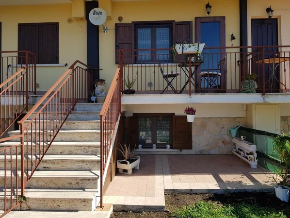 A two-story building with a balcony, a staircase, and a small outdoor seating area.
