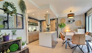 A modern kitchen with a central island, a dining area with a table and chairs, and a living space with a sofa and decorative items.