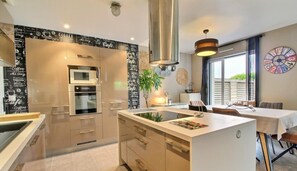 A modern kitchen with a central island, stainless steel appliances, and a dining area with a view.