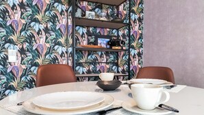 A dining area with a round table set for two, featuring plates, a cup, and cutlery. A bookshelf with decorative items is in the background. - Lovely apartment in Oostende with WiFi (Oostende)