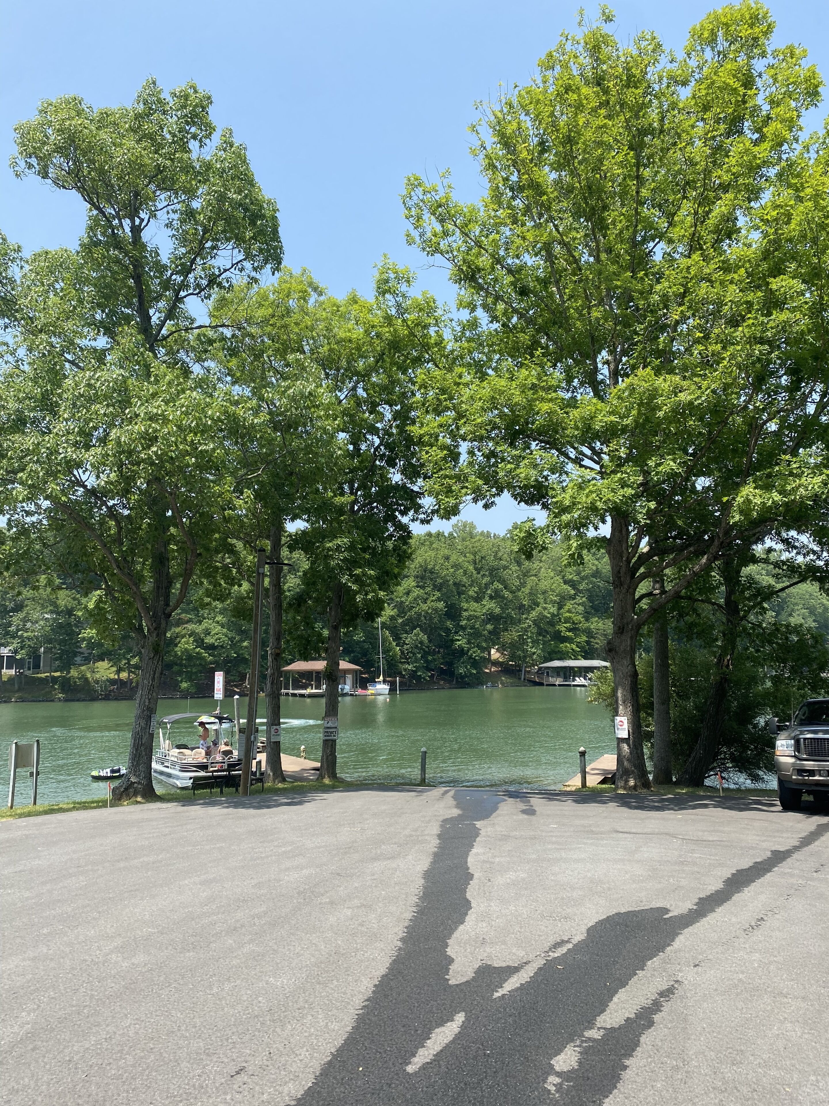 Un estacionamiento junto al lago con árboles, un muelle y barcos.