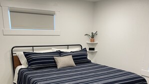 Una cama bien hecha con una colcha a rayas, un cabecero de madera y una pequeña planta en la mesita de noche.