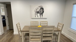 Un comedor con una mesa y sillas de madera, una obra de arte blanco y negro en la pared, y una ventana a la derecha.