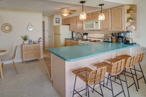 A kitchen with a central island, bar stools, wooden cabinets, a microwave, and various appliances.