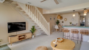 A modern living room with a staircase, a TV, a dining area, and a kitchen. - Charming Brigantine Condo Rental: Steps to Beach! (Brigantine)