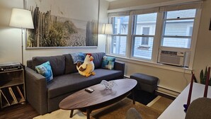 A living room with a sofa, a coffee table, a lamp, and a window with blinds. - Newly renovated apartment in the heard of Provincetown (Provincetown)