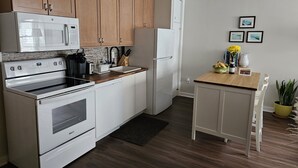 A compact kitchen with wooden cabinets, a white refrigerator, a microwave, and a stove. There is a small dining table with chairs and a potted plant. - Newly renovated apartment in the heard of Provincetown (Provincetown)