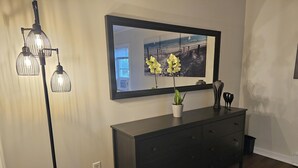 A modern living room with a dark wooden dresser, a large mirror, and a floor lamp with three light bulbs. - Newly renovated apartment in the heard of Provincetown (Provincetown)