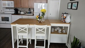 A compact kitchen with wooden cabinets, a white refrigerator, a microwave, and a sink. There is a wooden dining table with two chairs and a vase with yellow flowers. - Newly renovated apartment in the heard of Provincetown (Provincetown)