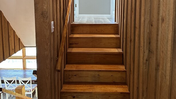 A wooden staircase leading to a room with a white wall and a decorative tree.