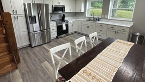 A modern kitchen with white cabinets, stainless steel appliances, and a wooden dining table with a patterned runner.