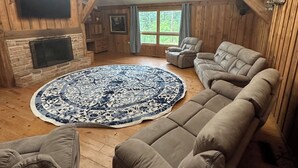 A cozy living room with a large round rug, leather sofas, a fireplace, a mounted TV, and a ceiling fan.