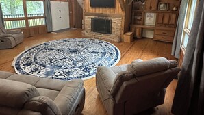 A cozy living room with a stone fireplace, wooden beams, a large round rug, and leather sofas.