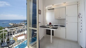 A compact kitchen with white cabinets and a small countertop, overlooking a scenic harbor with boats and yachts.