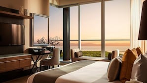 Une chambre d’hôtel moderne dotée d’un grand lit, d’un bureau et d’une télévision. Elle offre une grande fenêtre avec vue sur l’océan et les montagnes.