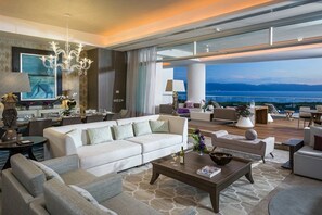 Un vaste espace de vie comprenant un grand canapé blanc, une table basse et une vue sur la mer.