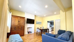 Ein Wohnzimmer mit blauem Sofa, Holzschrank, Kamin und Essbereich mit Tisch und Stühlen.