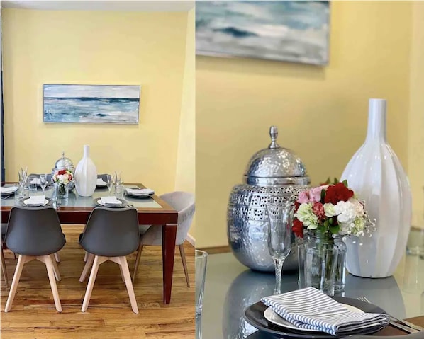 A dining area with a table set for two, a vase with flowers, and a decorative silver container.