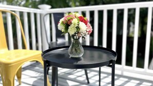 Ein runder Tisch mit Blumen in einer Vase auf einem Balkon mit weißer Reling.