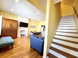 A spacious living room with a wooden floor, a blue sofa, a wooden cabinet, and a fireplace.