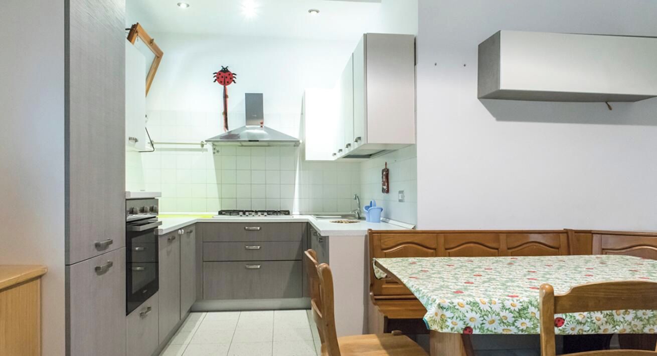 A compact kitchen with a stove, oven, and cabinets, a dining table with chairs, and a hanging plant.