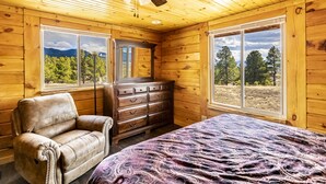 A wooden cabin room with a bed, a dresser, and a leather chair. - Mountain House Sleeps 18, Mins to Ski, Hike, Golf, Fish; Generator;  Fenced Yard (Angel Fire)