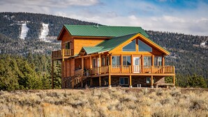 A log cabin with a green roof, multiple balconies, and a view of a snowy mountain range. - Mountain House Sleeps 18, Mins to Ski, Hike, Golf, Fish; Generator;  Fenced Yard (Angel Fire)