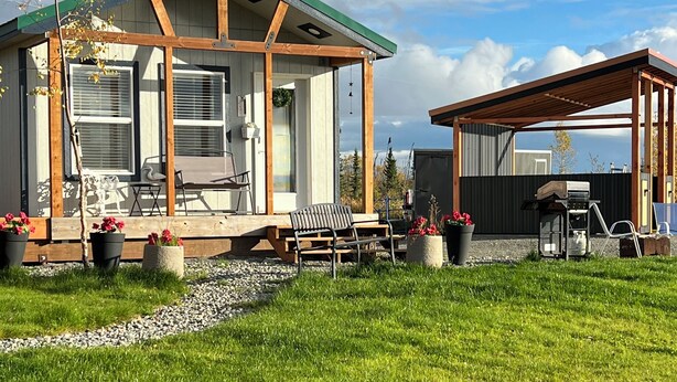 Una casa con veranda coperta, zona barbecue e giardino.